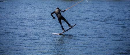 The man does wakeboarding on the water in the summer in a helmet and wetsuit.