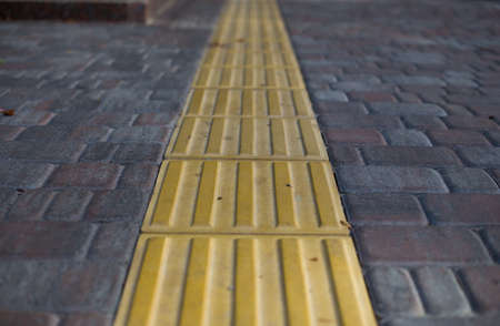 Yellow tactile tiles for the blind and visually impaired on the sidewalk in the city on the street