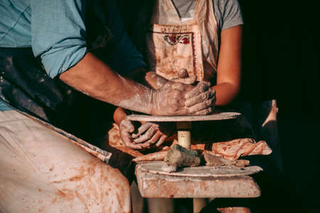 An experienced potter teaches an apprentice to work with clay and a potter's wheel