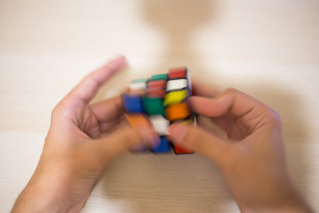 Hand holds a colored puzzle Rubik's cube three by three lies on a wooden table
