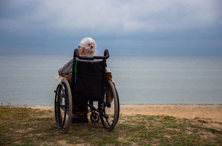 Elderly grandmother sits in a wheelchair by the seaの写真素材