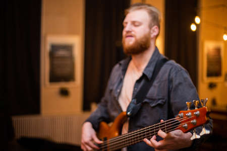 A young guy with a beard plays a bass guitar with five strings