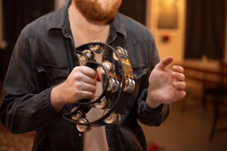 A young guy with a beard plays the tambourine