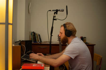 A young guy with a beard sings into a studio microphone with a pop filter