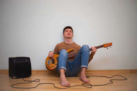 Young man playing on a guitar with wall on the background