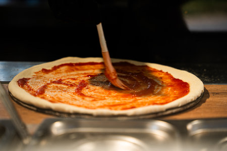Chef in black gloves artistically spreads tomato sauce on pizza dough.の写真素材