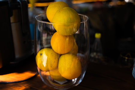 A vase full of ripe oranges bathed in natural sunlight on a wooden countertop, with a blurred background creating a cozy atmosphere.の写真素材