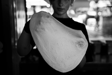 A chef stretches fresh pizza dough, captured in monochrome detail.