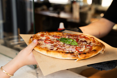 Hand presenting a freshly cooked pizza with gourmet toppings.の写真素材