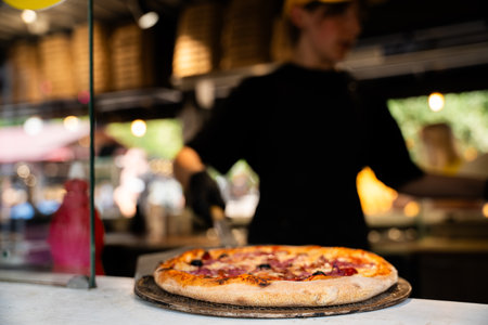 Close-up of a freshly baked artisan pizza with the chef and restaurant interior in the background, out of focusの写真素材