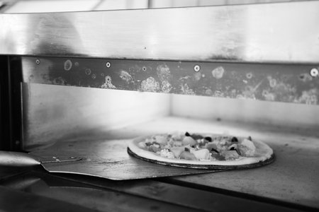 Monochrome image of a pizza with toppings on a peel at the oven's entrance.の写真素材