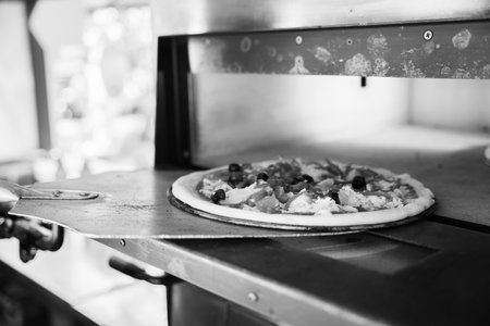 Monochrome image of a pizza with toppings on a peel at the oven's entrance.の写真素材