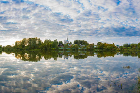 Lake with reflection of clouds and a church on the shore.の写真素材