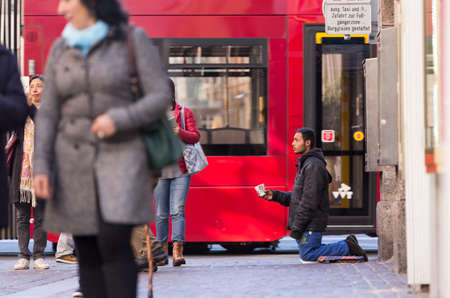 INNSBRUCK, AUSTRIA - NOVEMBER 1st 2015: Refugee begging for help in the streets of Innsbruck with people walking by.のeditorial素材