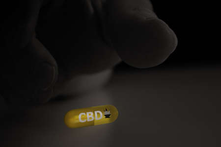 CBD capsule with writing and hemp leaf on the pill, and hand in black and white reaching for the tablet. 3D render.の写真素材