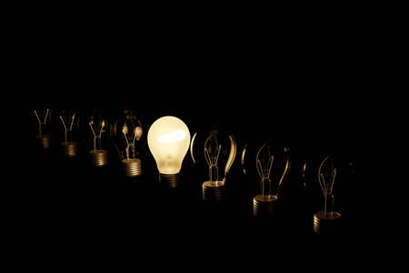 Line of light bulbs with middle light bulb shining bright illustrating having an idea. 3D render with black background.の写真素材