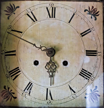 Old worn house clock with classic black numbers on cracked and ornate white dial and metal arrows.