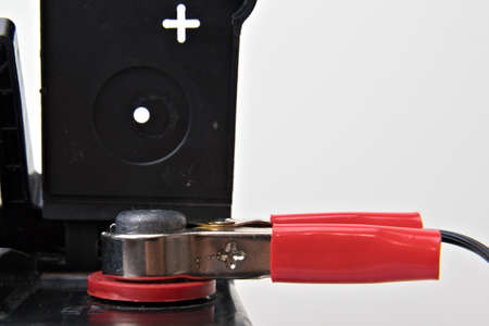 Red car battery clamp attached to a black 12V car battery on the positive connection. Close up on white.の写真素材