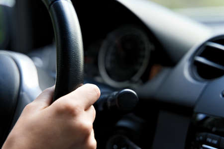 Female hand on steering wheel of a car while driving. Black interior.の写真素材