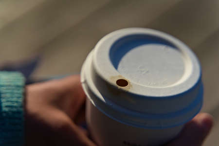 Lid of a paper coffee cup with small coffee stain. Held in hand by young female.の写真素材