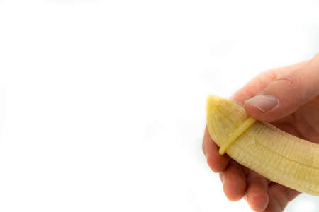 Male hand putting a condom on a banana imitating an erect penis. Isolated on white background. . High quality photoの写真素材