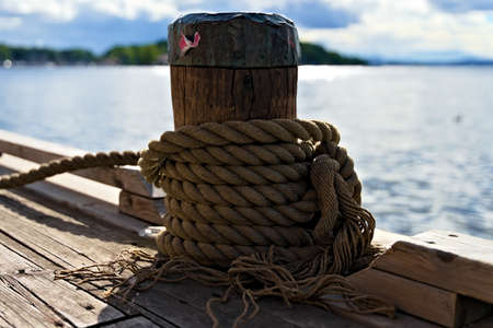 Maritime hemp rope moorings from a ship tied around an old wood bollard in the marina.の写真素材