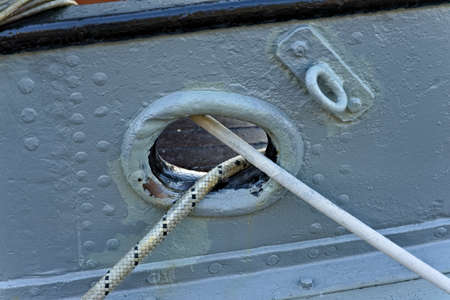 Mooring lines going from a cleat hole on a white steel ship at port.