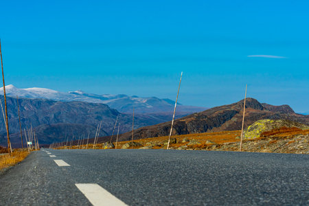 Asphalt road through the mountain highlands, with tall wooden marking sticks placed on the side....