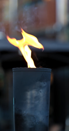 Black iron torch with yellow and orange live flame and blurred background.の写真素材