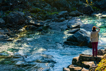 Female hiker standing on a cliff by a wild river and waterfall enjoying the view. . High quality photoの写真素材