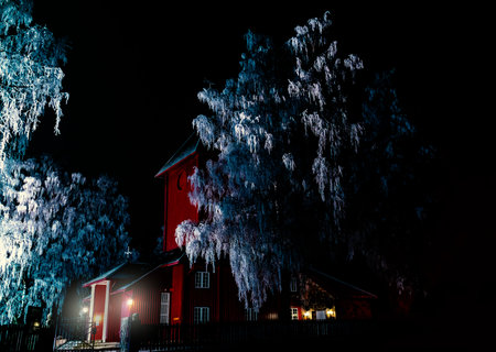 Idyllic red wooden church surrounded by frozen white trees in a winter wonderland at night. High quality photoの写真素材