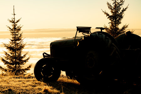Silhouette of an old tractor parked on a hilltop above dense fog in the valley below. . High quality photoの写真素材