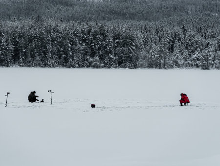 Two men fishing from the ice of a frozen lake covered in deep snow. High quality photoの写真素材