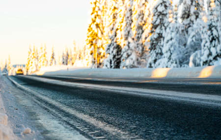 Traffic on an icy road running through a snow covered pine forest on a clear winters day. Shallow depth of field.の写真素材