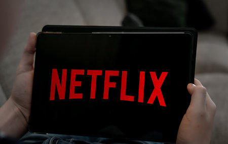 Hands holding tablet with Netflix logo on a black screen. Shallow depth of field. High quality photo