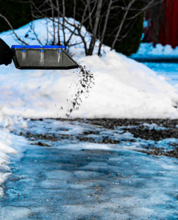Hand strewing gravel onto a frozen driveway on a cold winters day. Shallow depth of field. High quality photoの写真素材