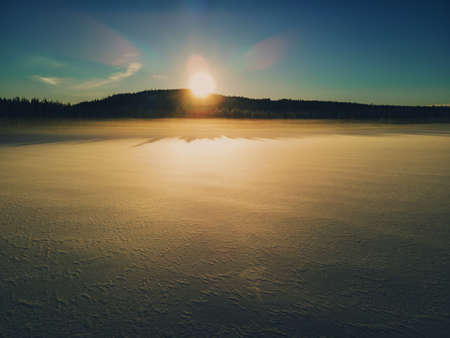 Sunset over the snowy ice of a frozen lake in the wild. Frozen cold fog. High quality photo