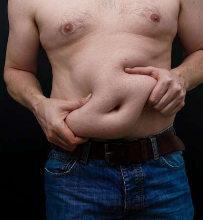 Man with extra weight on his belly grabs his skin. Isolated on black background. High quality photoの写真素材