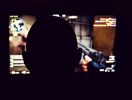 Silhouette of a person playing a 3D shooter game on a computer in a dark room. Shallow depth of...