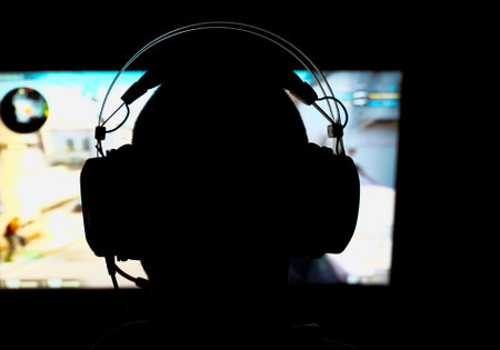 Silhouette of a person playing a 3D shooter game on a computer in a dark room. Shallow depth of...
