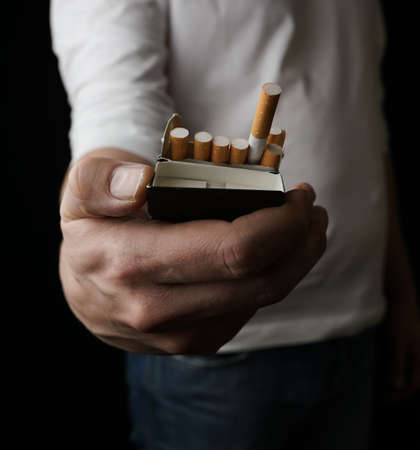 Person holding out a pack of cigarettes offering a smoke. Isolated on black background with shallow...