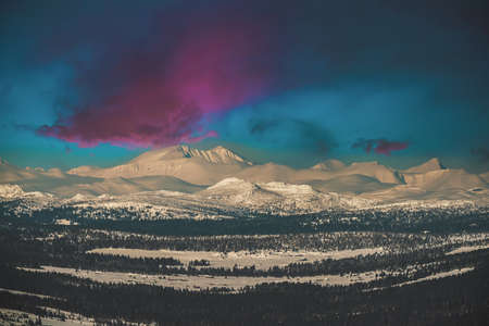 View over a majestic mountain wilderness landscape in winter with dramatic sunset clouds. High...