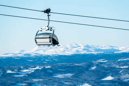 Empty ski lift on a cable with snow covered mountains in the background.の写真素材