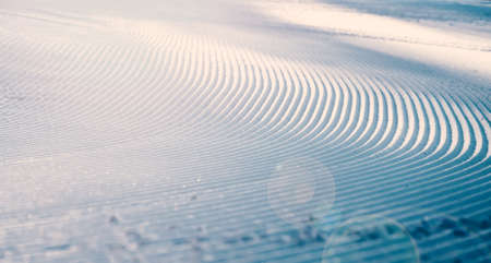 Close up of groomed tracks on a slope in a downhill ski resort on a sunny day. Shallow depth of field. High quality photoの写真素材