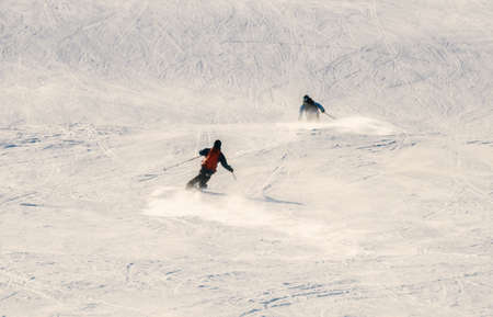 Two skiers speeding down a slope at a winter sports resort on a bright sunny day. High quality photoの写真素材