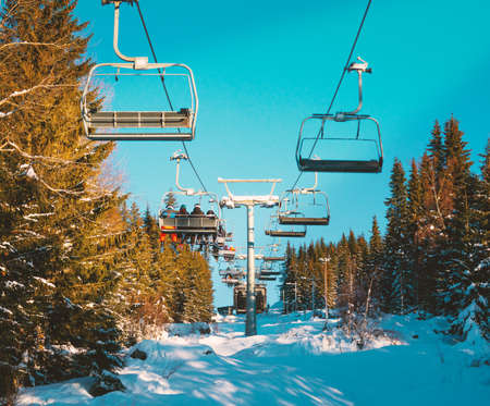 Cable chair lifts at a ski resort with skiers riding to the top of the slopes. High quality photoのeditorial素材