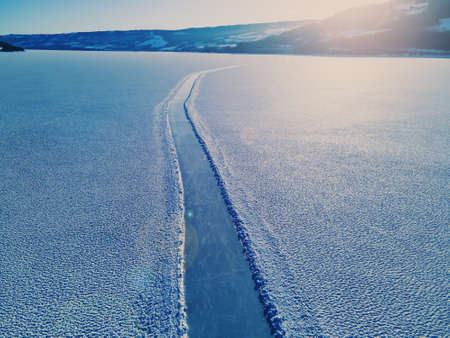 Ice skating road on the clear glassy ice of a large frozen lake with light snow on top of the ice. High quality photoの写真素材