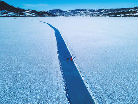 Ice skaters resting on a large frozen lake with clear glassy and cracked ice beneath the snow. High quality photoの写真素材