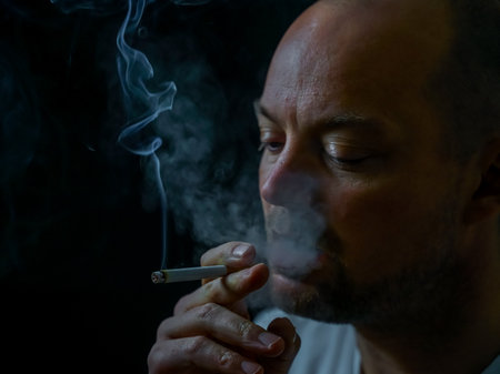 Man smoking a cigarette blowing out white smoke. Isolated on black background, shallow depth of...