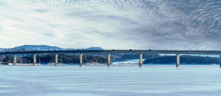 Panorama of a long bridge with traffic driving on it, spanning across a frozen bay on a clear cold winters day. High quality photoの写真素材